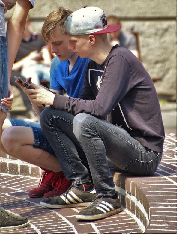 Jugendliche sitzen draußen auf dem Pausenhof mit ihren Smartphones